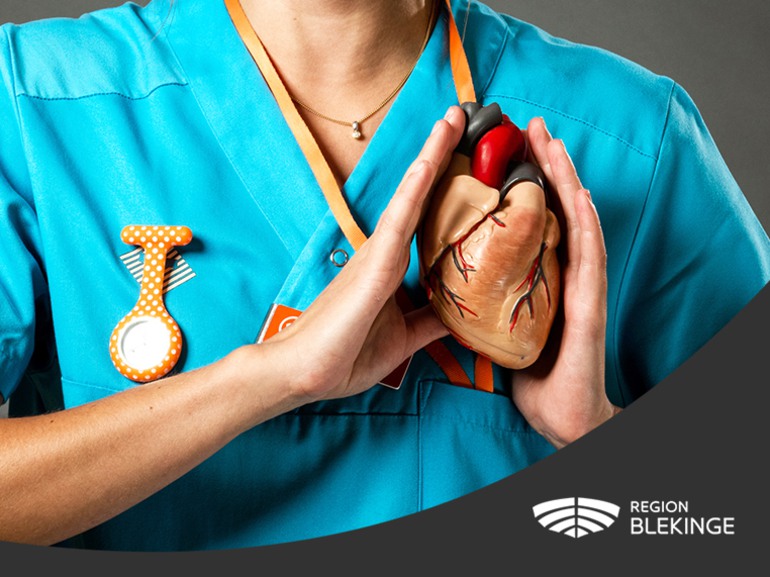 En sjuksköterska håller upp ett hjärta framför sig samt Region Blekinges logotyp.