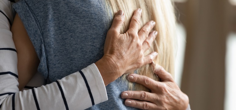 Två händer i bild som kramar om en annan person. Personen har grå tröja och blont hår. 