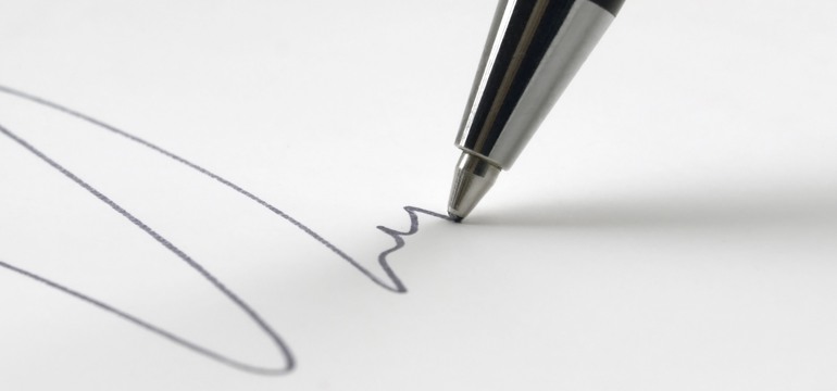 Närbild på spetsen av en svart bläckpenna som skriver på ett vitt papper.