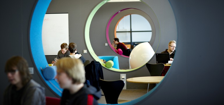Bild på personer som sitter vid bord i en högskolemiljö.