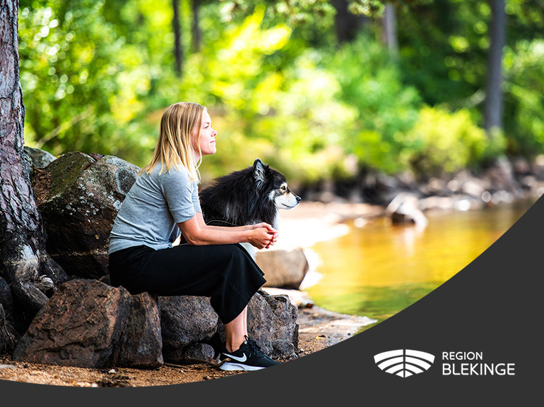 Region Blekinges logotyp med bild på en tjej som sitter med sin hund och tittar ut över sjö