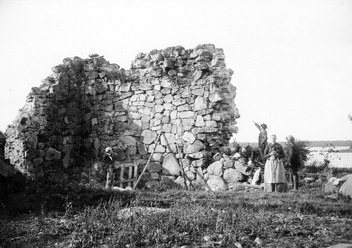 Äldre svartvitt foto med fyr människor runt en hög mur