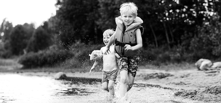 Två barn som springer i vattnet vid en strandkant.