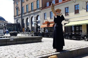 Kvinna i 1800-talskläder blåser i lur i stadsmiljö