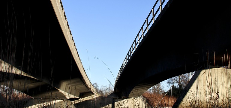 Bild på motorvägsbro underifrån, med blå himmel i bakgrunden.