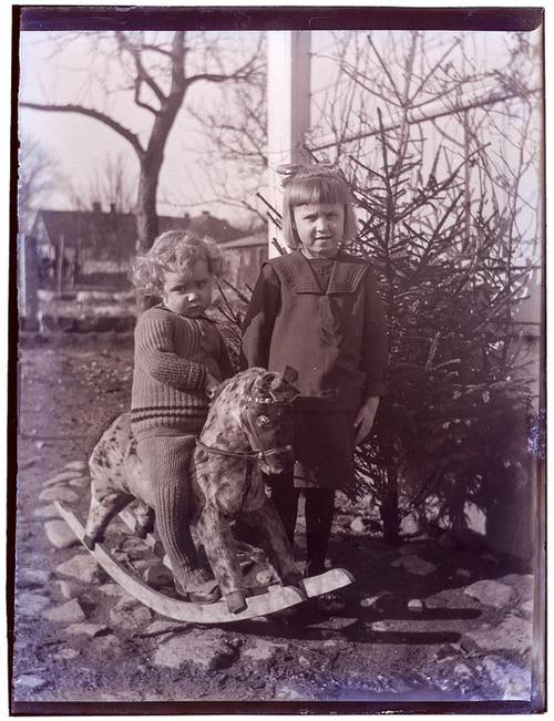Ett äldre svartvitt fotografi föreställande två barn och en gunghäst