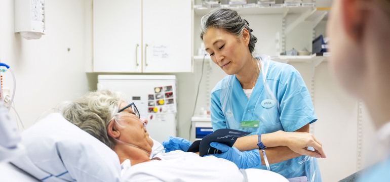 En undersköterska kontrollerar blodtrycket på en patient i en sjukhussäng.