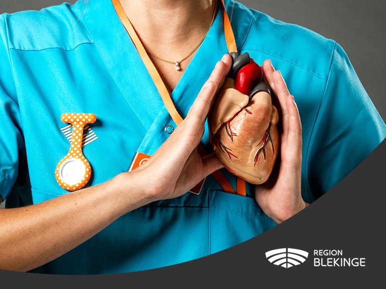 En sjuksköterska håller upp ett hjärta framför sig samt Region Blekinges logotyp.